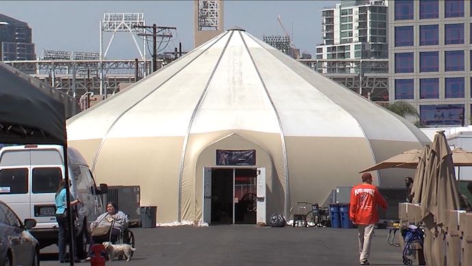 Large Silver Outdoor Round Popup Tent Homeless Shelter With People Walking In Foreground In San Diego