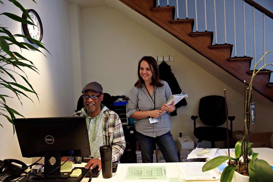 Two People In Office With Man Smiling On The Computer With A Woman Smiling And Standing Over The Man's Shoulder