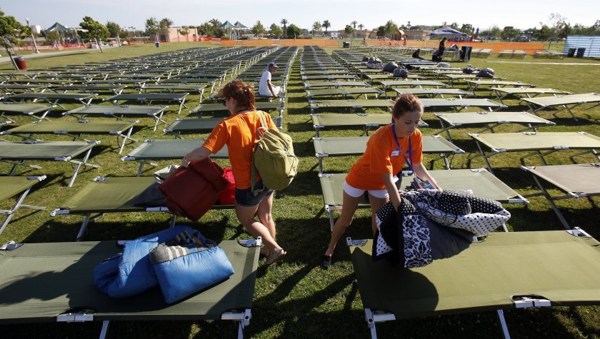 Two Girls Wearing Orange Shirts Laying Out Blankets On Outdoor Cots On A Football Field For Sleepless San Diego